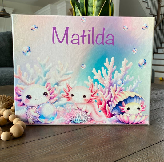 Personalized pastel canvas featuring the name "Matilda" in a playful purple font, surrounded by an enchanting underwater scene. Three adorable, pink axolotls with expressive eyes are depicted among soft-hued coral, shimmering bubbles, and a pearl-filled seashell. The dreamy watercolor-style artwork creates a whimsical oceanic theme, perfect for kids' room decor, nursery art, or a unique custom gift.
