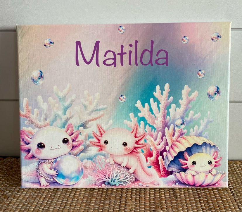 Personalized pastel canvas featuring the name "Matilda" in a playful purple font, surrounded by an enchanting underwater scene. Three adorable, pink axolotls with expressive eyes are depicted among soft-hued coral, shimmering bubbles, and a pearl-filled seashell. The dreamy watercolor-style artwork creates a whimsical oceanic theme, perfect for kids' room decor, nursery art, or a unique custom gift.